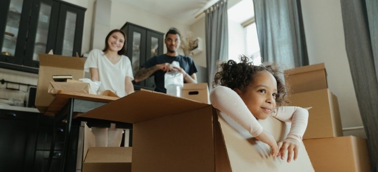 Girl sitting in a cardboard box parents in the back packing inventory